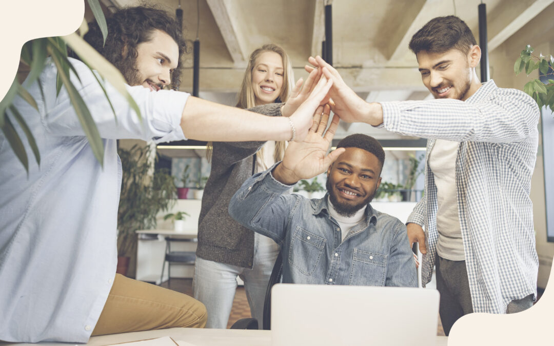 Group of four coworkers in an office giving a high-five around a laptop.